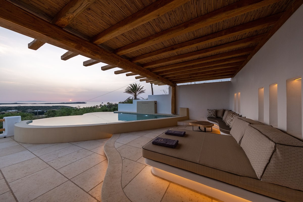 A modern outdoor seating area with a pool, wooden ceiling, and a view of the landscape.