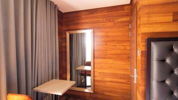 A room with a wooden floor, a bed, a chair, a table, and a mirror.