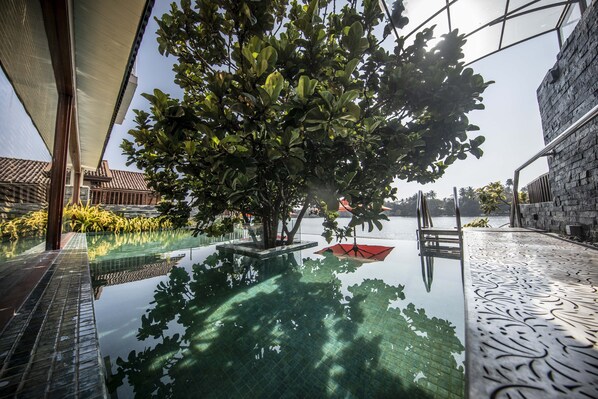 Uma área de piscina interior tranquila, com água cristalina, rodeada por vegetação exuberante e uma parede de pedra.