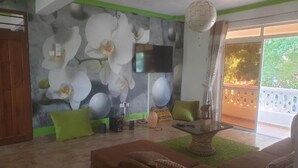 Een woonkamer met een grote bloemenmuur, een flatscreen televisie, een bank en een balkon met een balustrade.