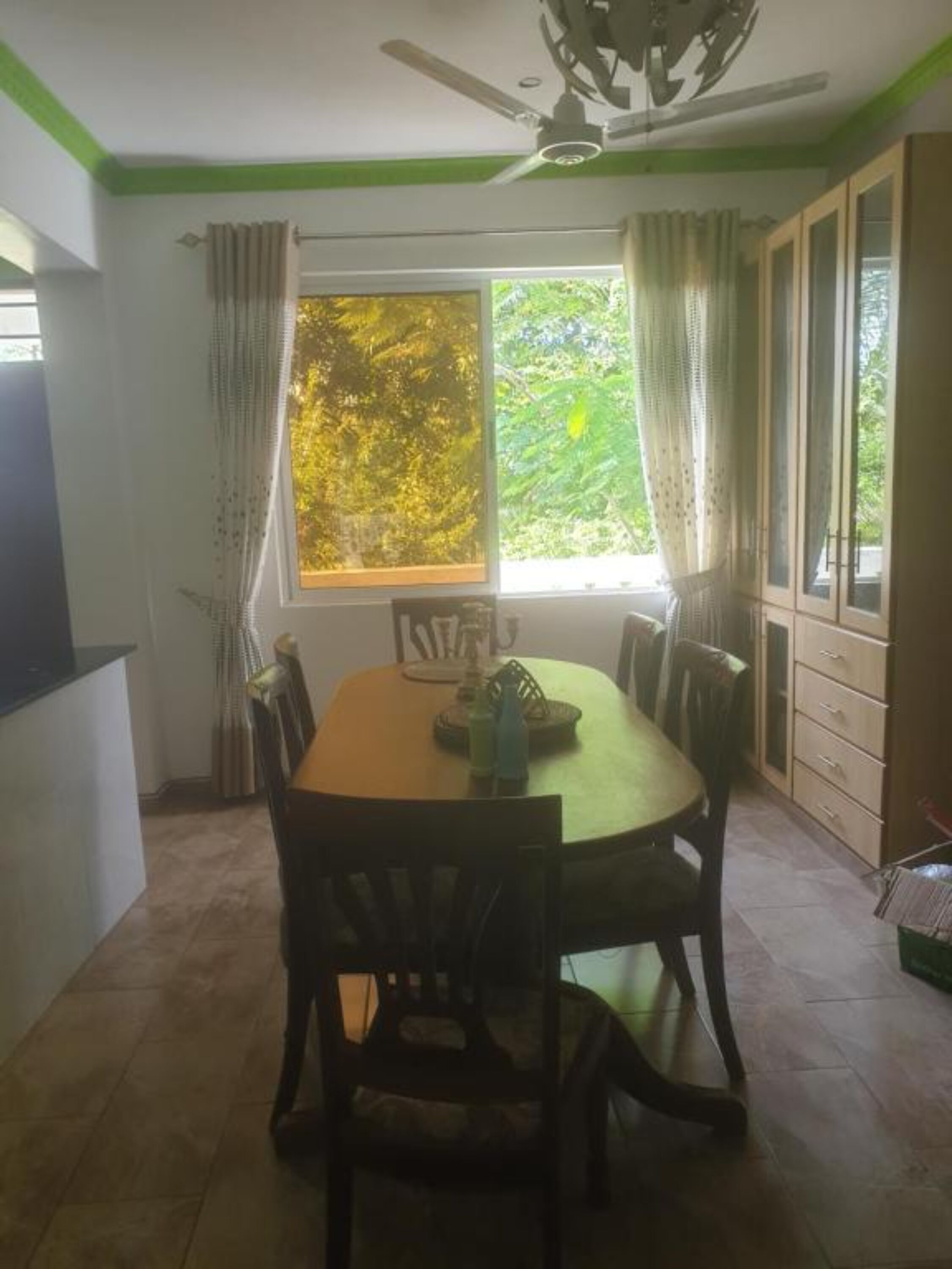 A dining area with a round table and chairs, a ceiling fan, and a window with curtains.