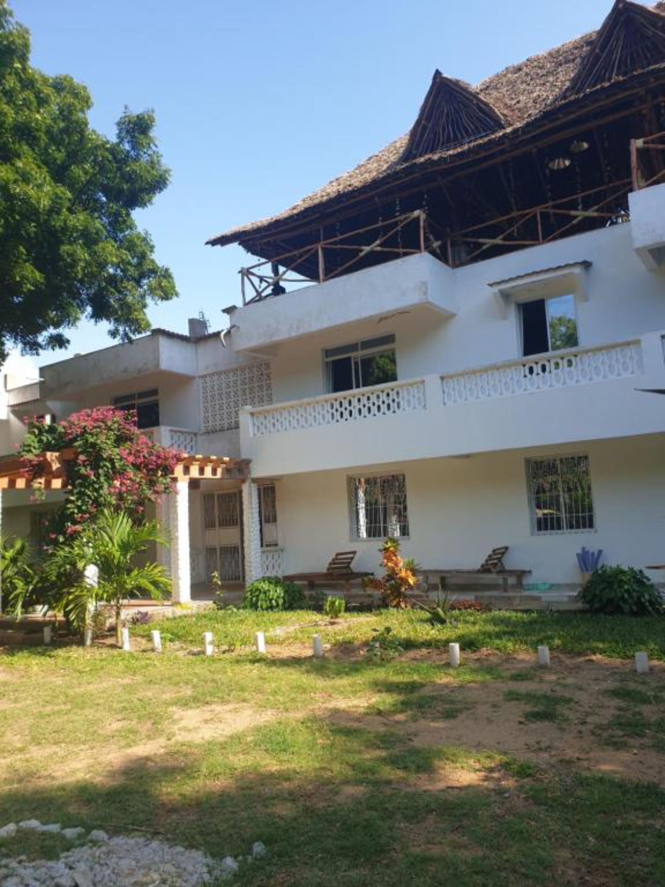 A two-story building with a balcony on the second floor, a covered patio area, and a garden with a lawn and some plants.