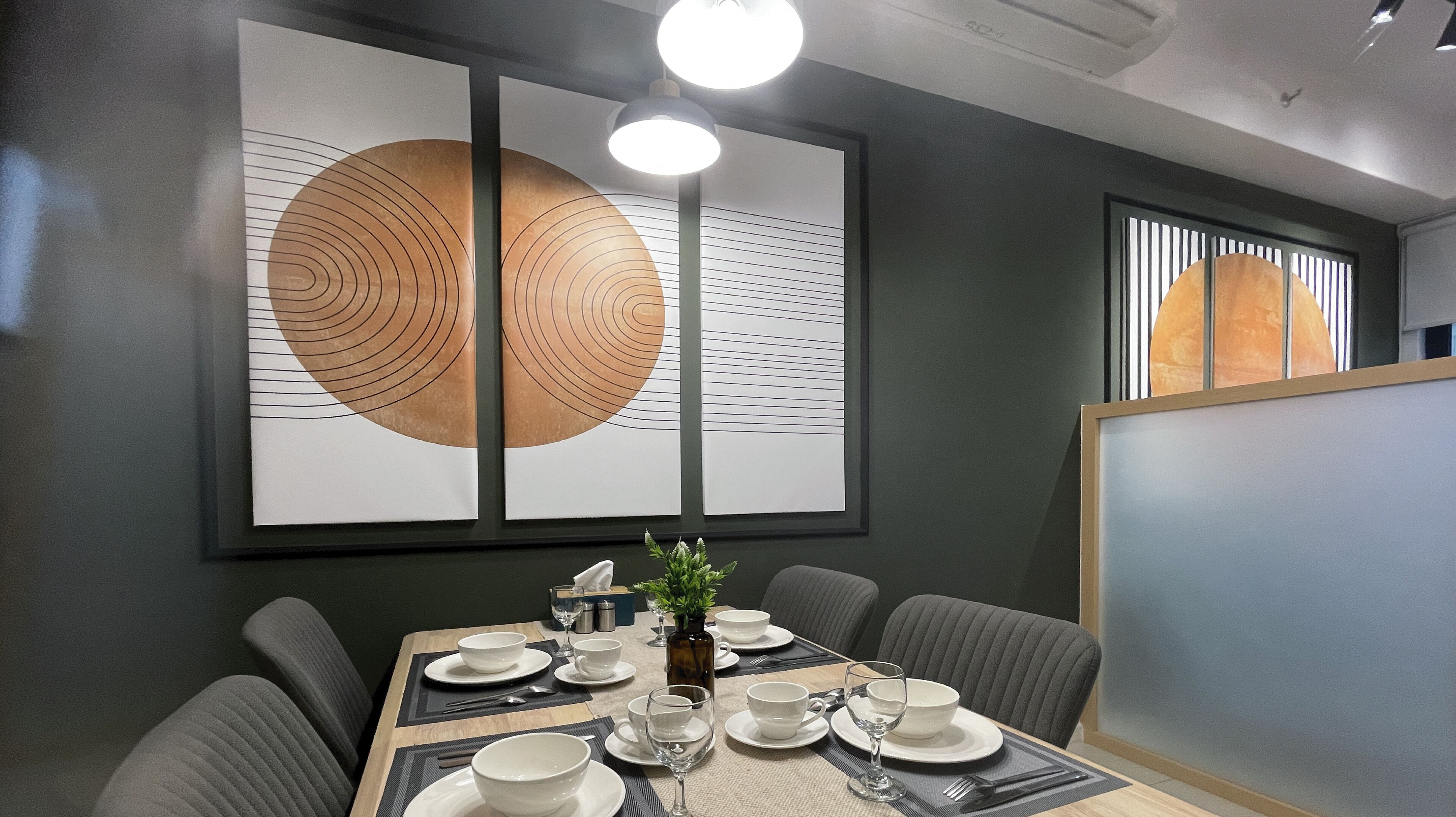 Un coin repas avec une table dressée pour six personnes, comprenant des assiettes, des bols et des verres. Deux grandes œuvres d'art abstrait ornent le mur au-dessus de la table.