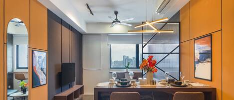 Un espace repas moderne avec vue sur la ville, doté d’un ventilateur de plafond et d’une table à manger agrémentée de verres et d’un vase de fleurs.
