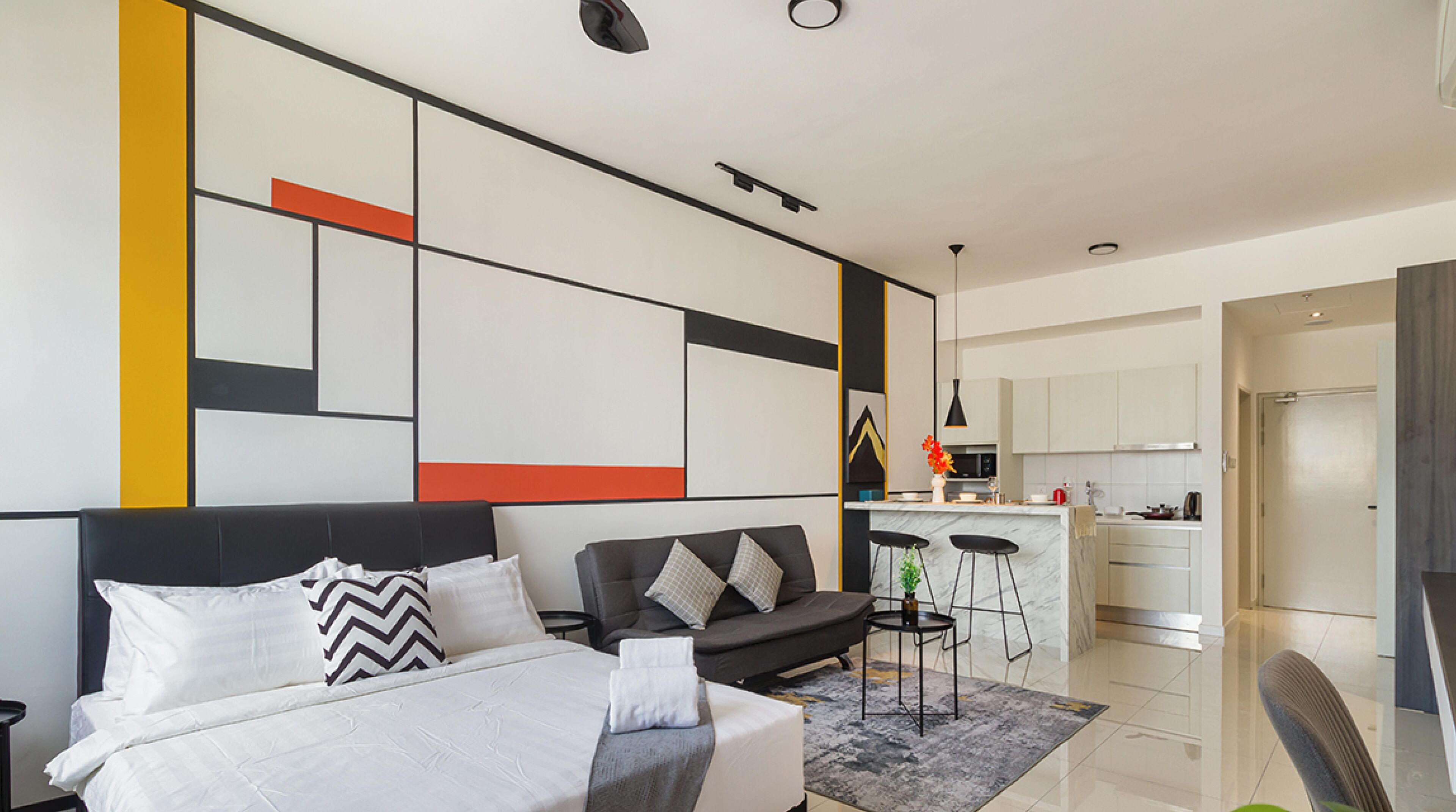 Un dormitorio moderno con una cama grande, un sofá y una cocina visible a través de una puerta abierta.