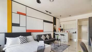 Un dormitorio moderno con una cama grande, un sofá y una cocina visible a través de una puerta abierta.
