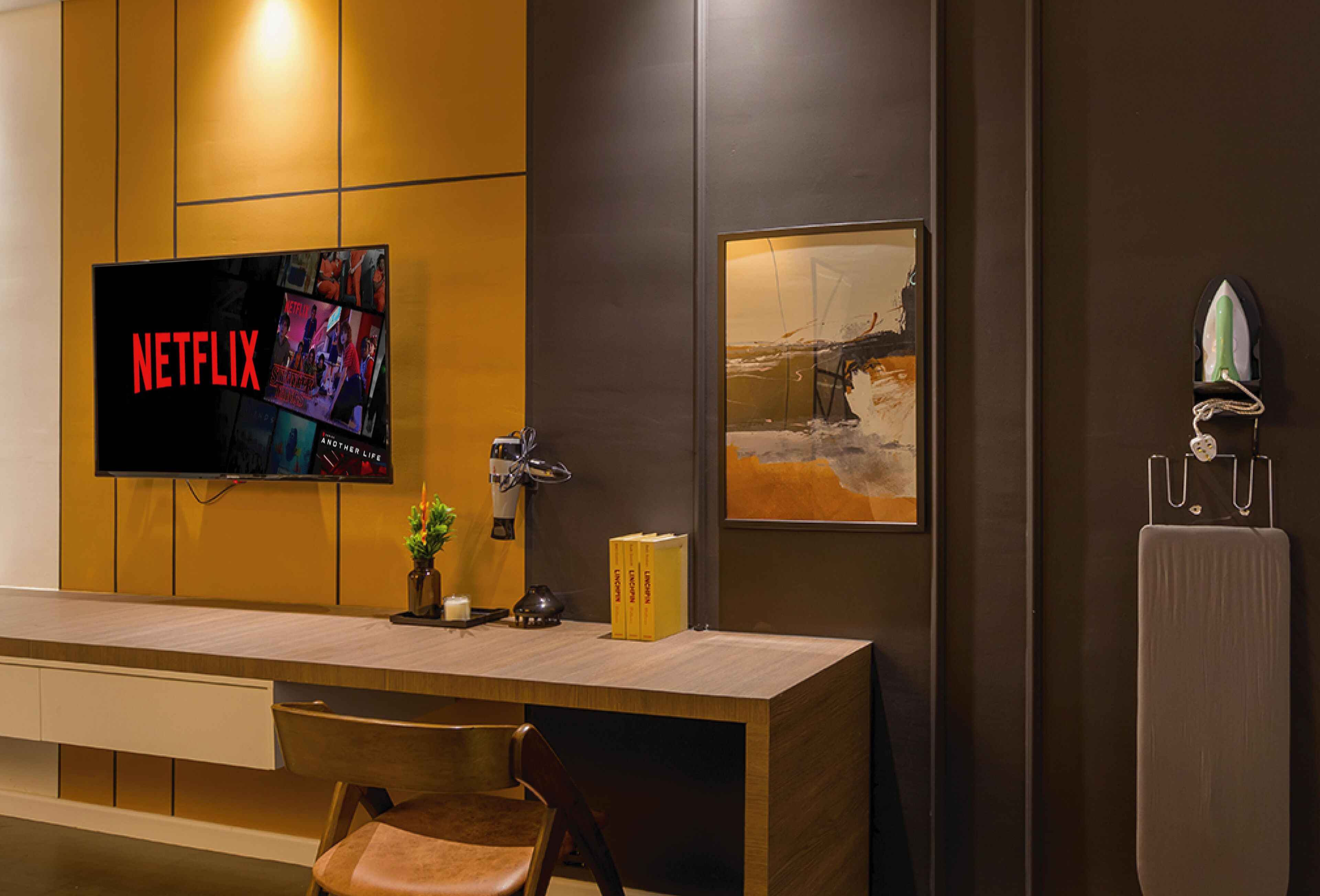 Ein modernes Hotelzimmer mit einem Holztisch, einem Flachbildfernseher, der Netflix zeigt, einem Gemälde und einem Bügeleisen an der Wand.