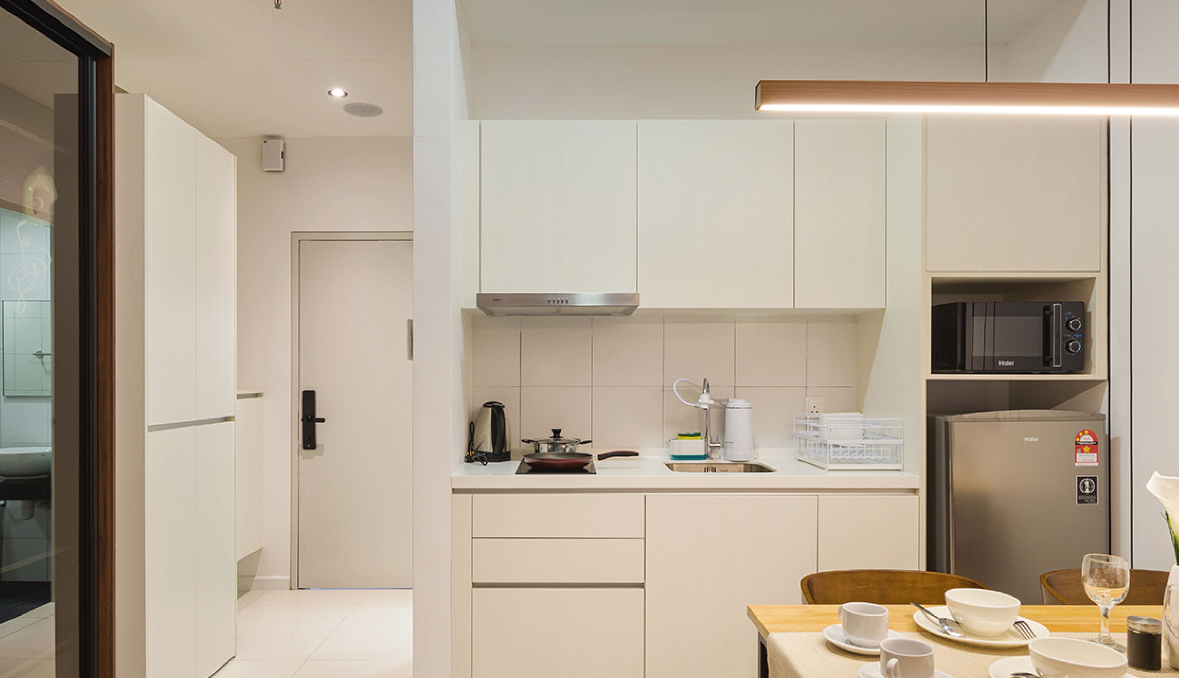 A modern kitchen with white cabinetry, a microwave, and a refrigerator. There is a dining area with a table set for two.