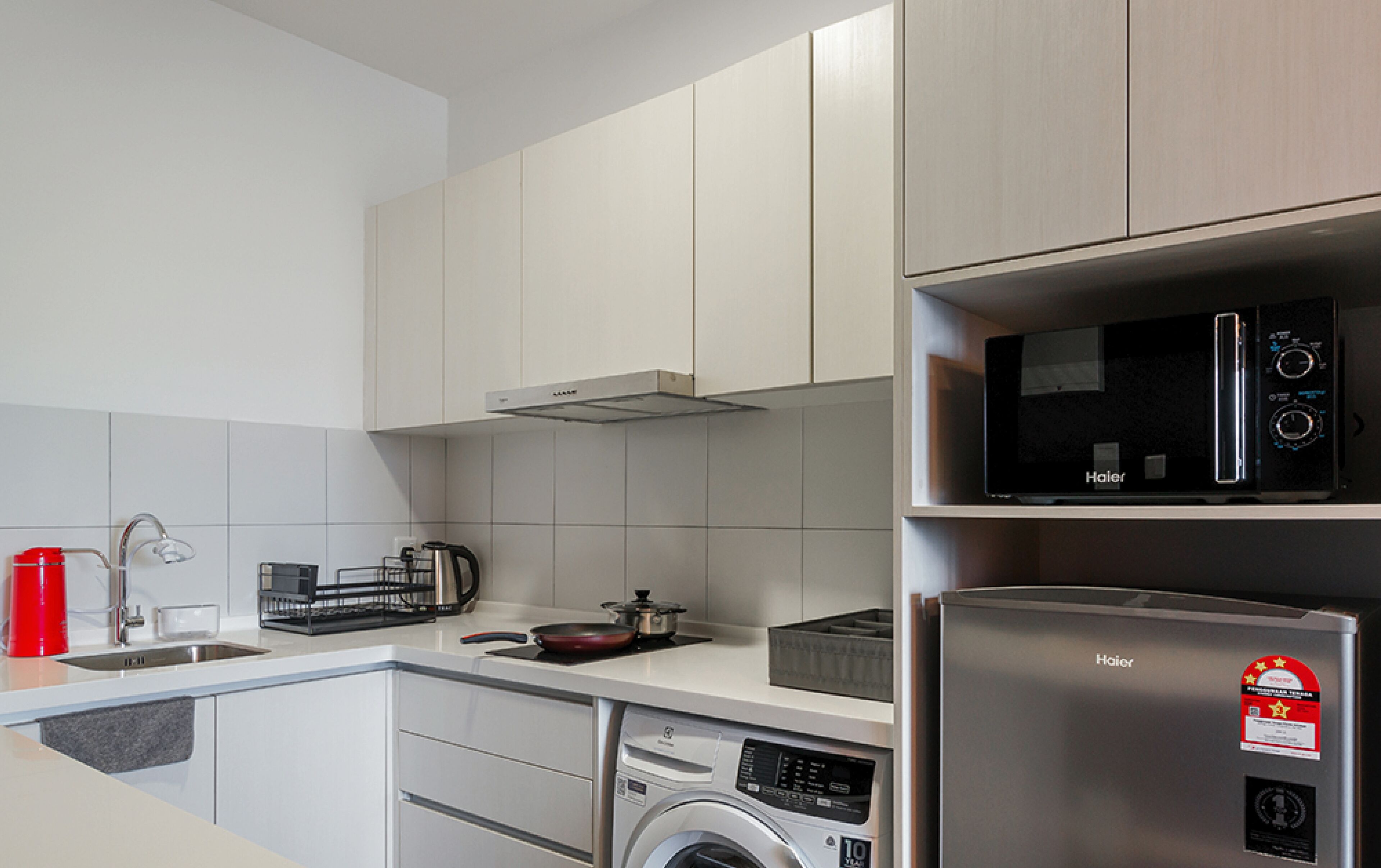 Een moderne keuken met witte kasten, een roestvrijstalen koelkast, een magnetron, een wasmachine en een koffiezetapparaat.