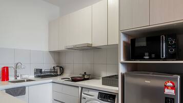 Een moderne keuken met witte kasten, een roestvrijstalen koelkast, een magnetron, een wasmachine en een koffiezetapparaat.