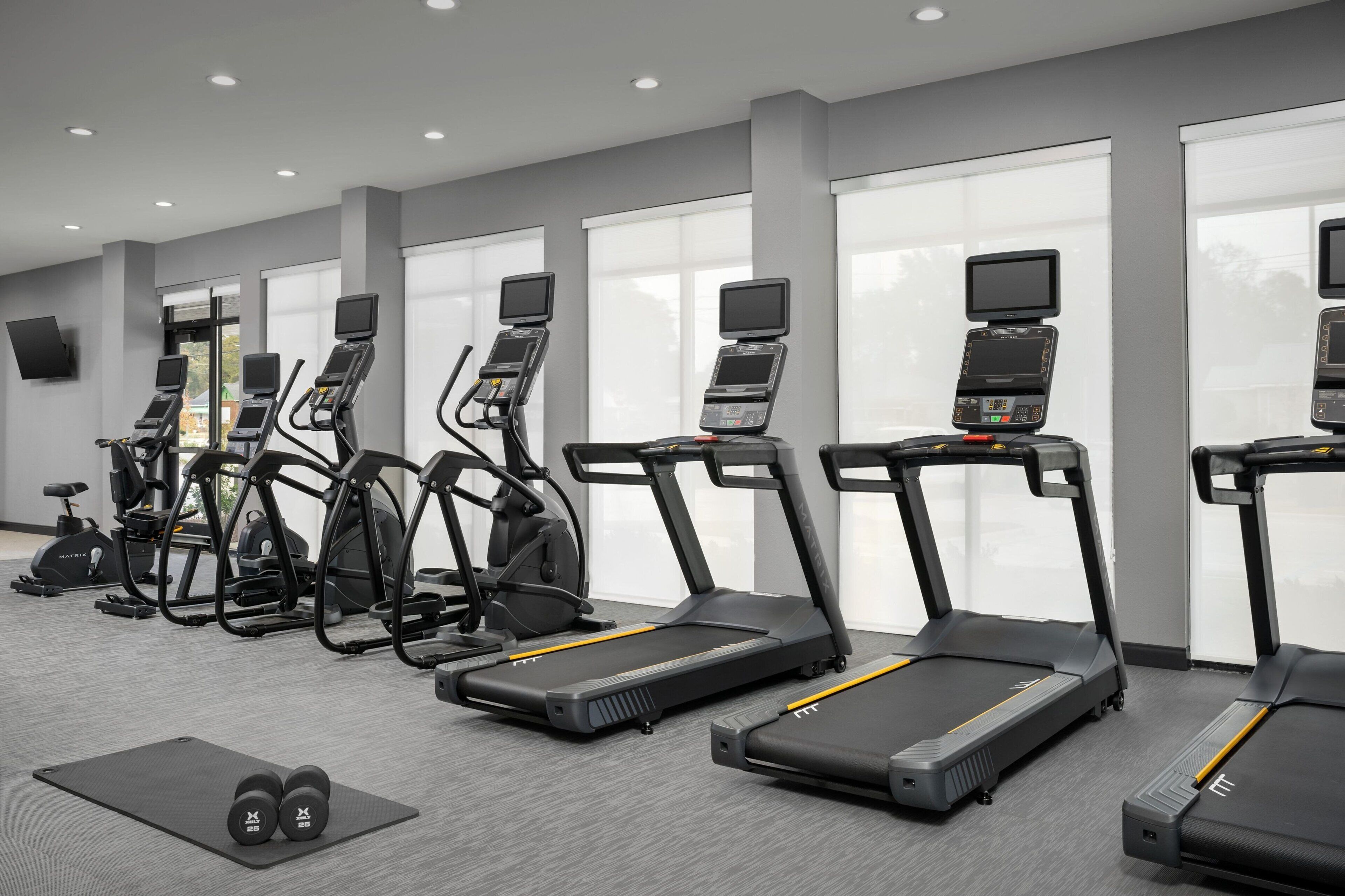 Une salle de sport équipée de tapis de course, de vélos elliptiques et d’haltères.