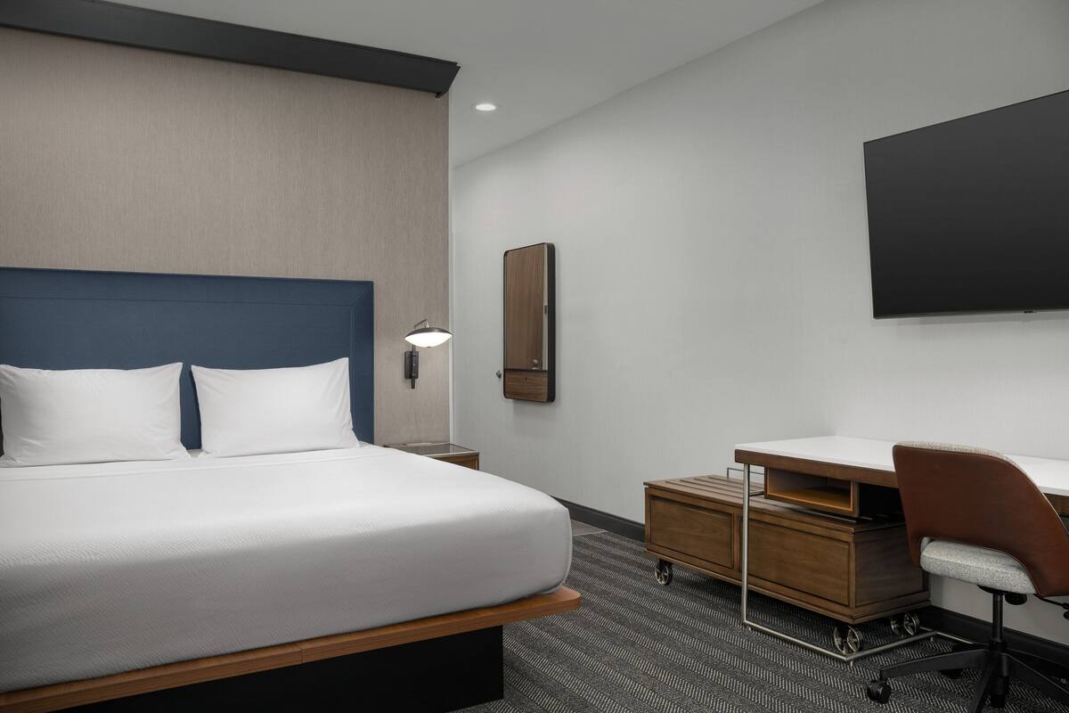 Une chambre d’hôtel moderne équipée d’un grand lit, d’un bureau, d’une chaise, d’un téléviseur à écran plat et d’une petite armoire.
