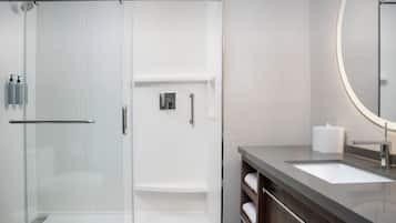 A modern bathroom with a glass-enclosed shower, a vanity with a sink, and a mirror with a circular frame.
