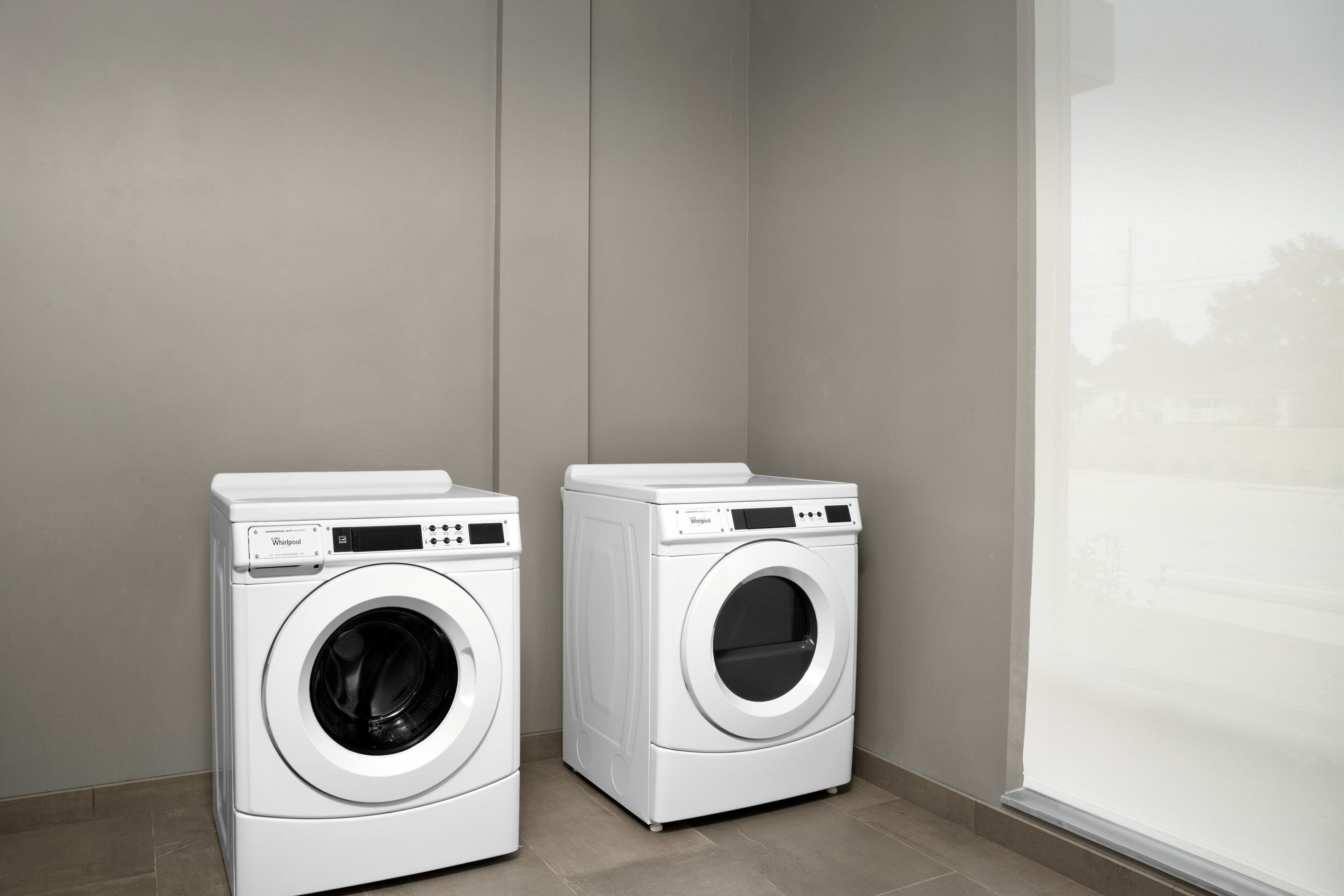 Two white Whirlpool front-loading washing machines in a corner of a room with a large window.