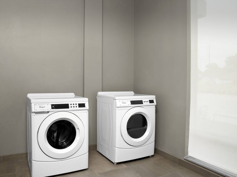 Two white Whirlpool front-loading washing machines in a corner of a room with a large window.
