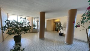 Un espacio interior amplio con suelo de baldosas, grandes columnas y plantas en macetas.