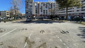 Un estacionamiento con varios autos, un edificio de varios pisos y balcones, y algunos árboles.
