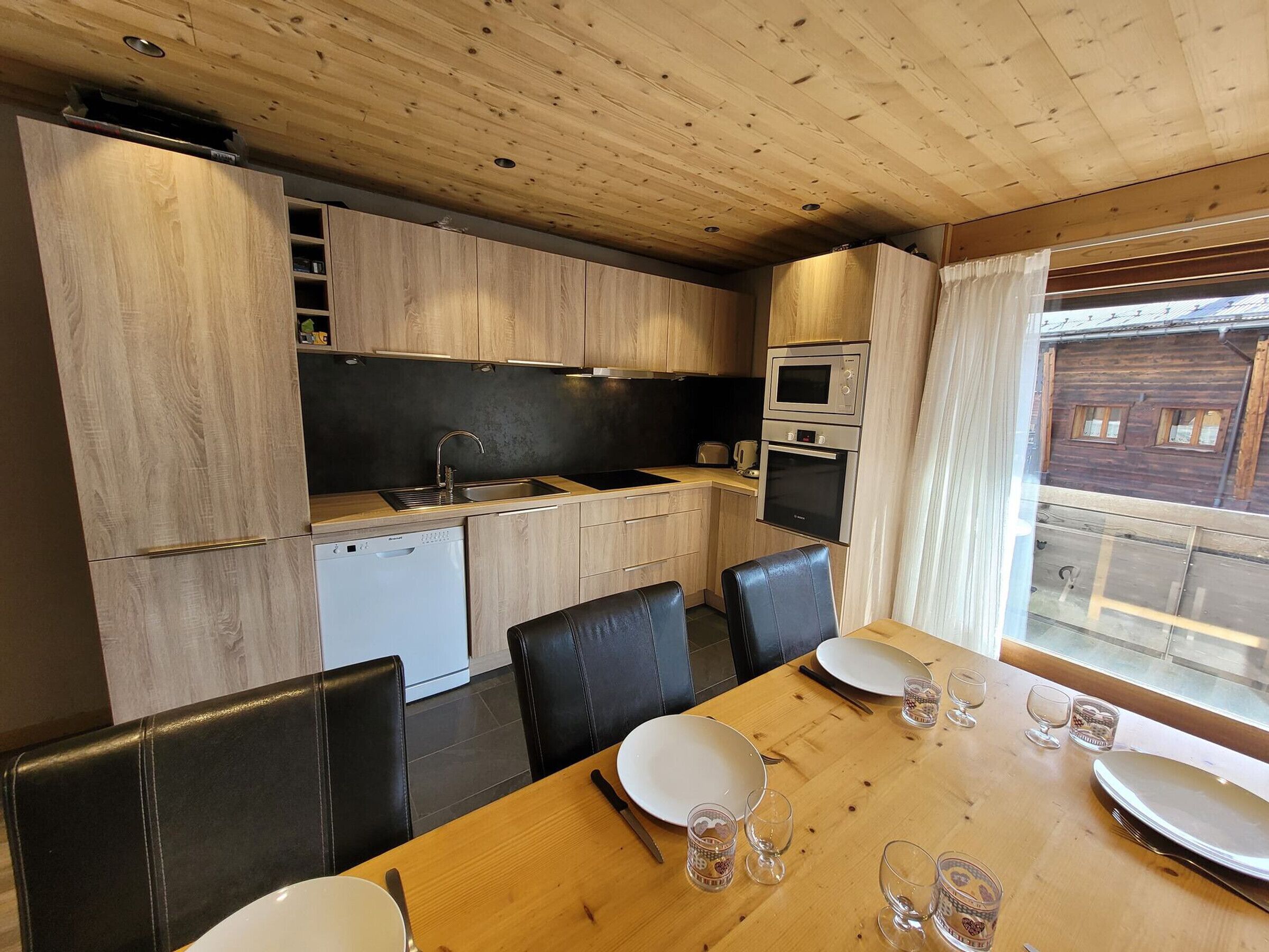 A compact kitchen with wooden cabinets, a built-in oven, and a dining area with a wooden table and black chairs.