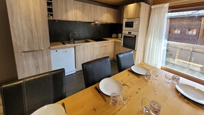 A compact kitchen with wooden cabinets, a built-in oven, and a dining area with a wooden table and black chairs.