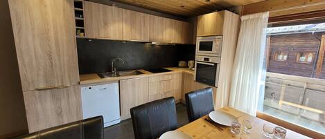 A compact kitchen with wooden cabinets, a built-in oven, and a dining area with a wooden table and black chairs.