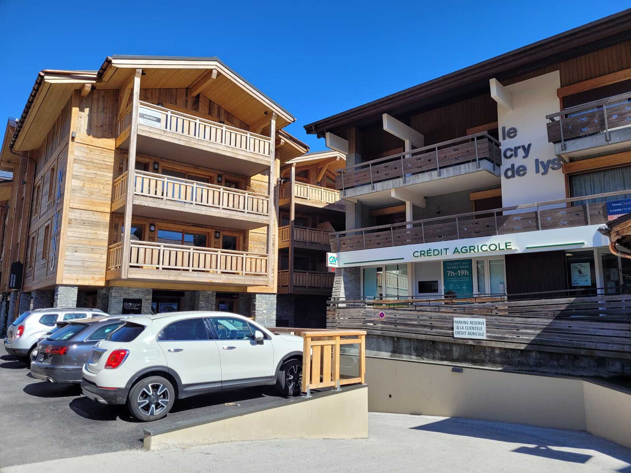 A multi-story wooden building with balconies, a sign for 'le cry de lys', and a 'CRÉDIT AGRICOLE' bank.