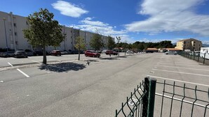 A parking lot with multiple cars, a fence, and buildings in the background. - Charming air-conditioned studio with wifi and parking 100m from the beach (Saint-Cyprien)