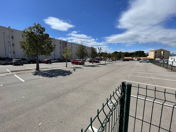 Un estacionamiento con varios coches, una valla y edificios al fondo.