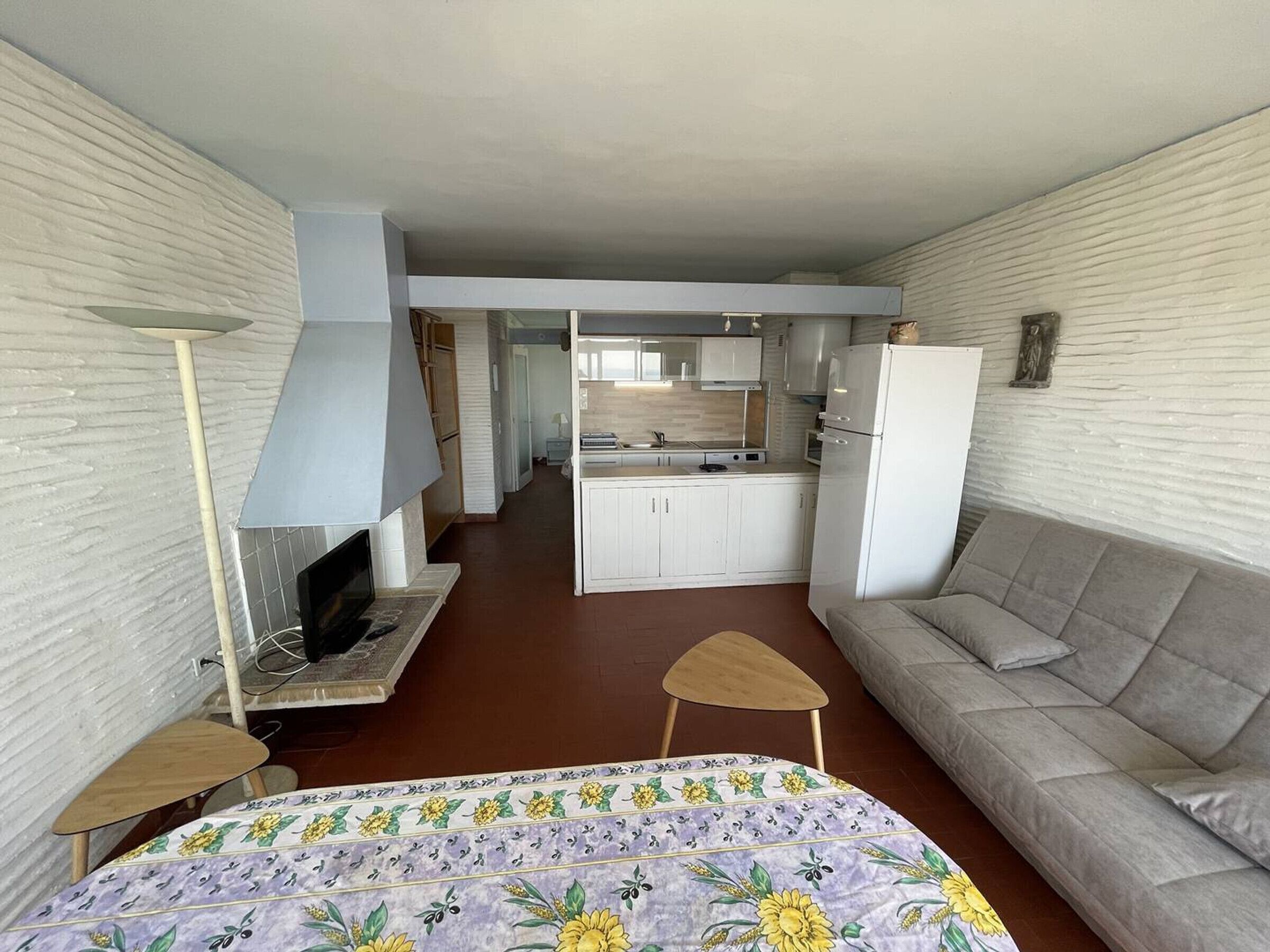 En kompakt opholdsstue med sofa, lille bord, tv og tekøkken.