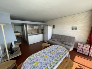 A compact room with a kitchenette, a sofa, a bed with a floral bedspread, and a small table.