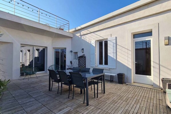A patio with a table and chairs, a sliding glass door, and a balcony with a railing.