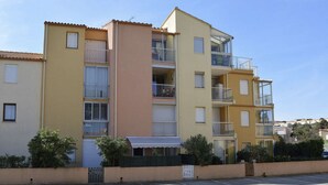 A multi-story residential building with balconies and a parking area in front.