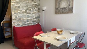 A compact room with a red sofa, a white table set for dining, and a stone-patterned wall.