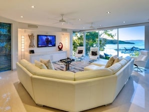 A modern living room with a large sectional sofa, a flat-screen TV, and a view of the sea.