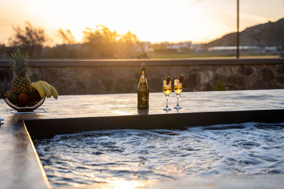 Escena junto a la piscina con un frutero, una botella y dos vasos de una bebida.