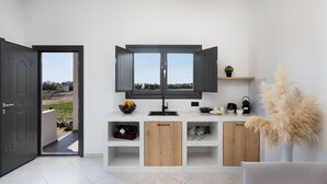 A modern living room with a TV, wooden cabinets, a shelf with decorative items, and a door leading outside. - Almira Luxury Suites (Santorini)