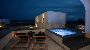 A modern outdoor relaxation area with a hot tub, two wooden lounge chairs, and ambient lighting. - Almira Luxury Suites (Santorini)