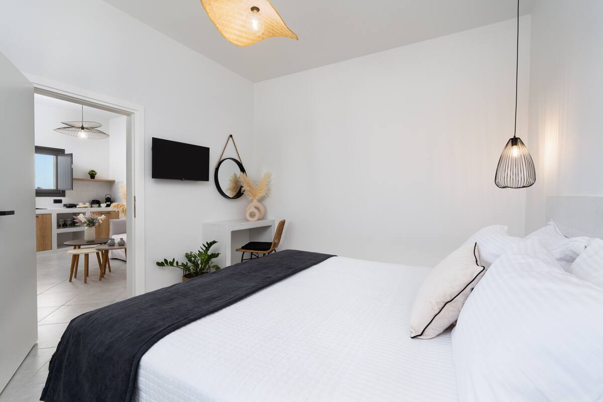 Un dormitorio moderno con una cama grande, un escritorio y una silla. Hay un televisor en la pared y una lámpara colgante.