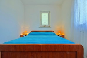 Een slaapkamer met een houten bed, twee bedlampen, een raam met zonwering en een nachtkastje.