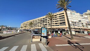 Et hotel med flere etager, altaner, et gågadeområde med palmer og en klar blå himmel.
