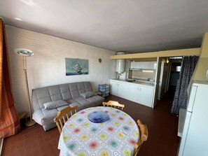 Un espacio habitable compacto con sofá, una mesa de comedor con mantel colorido, kitchenette y un cuadro en la pared.