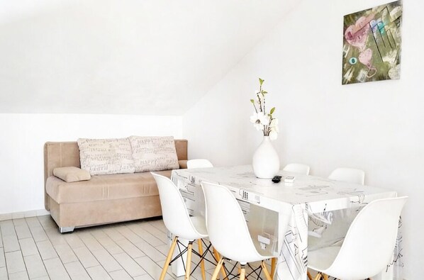 Uma área de refeições moderna e minimalista, com uma mesa branca, cadeiras brancas e um sofá bege.