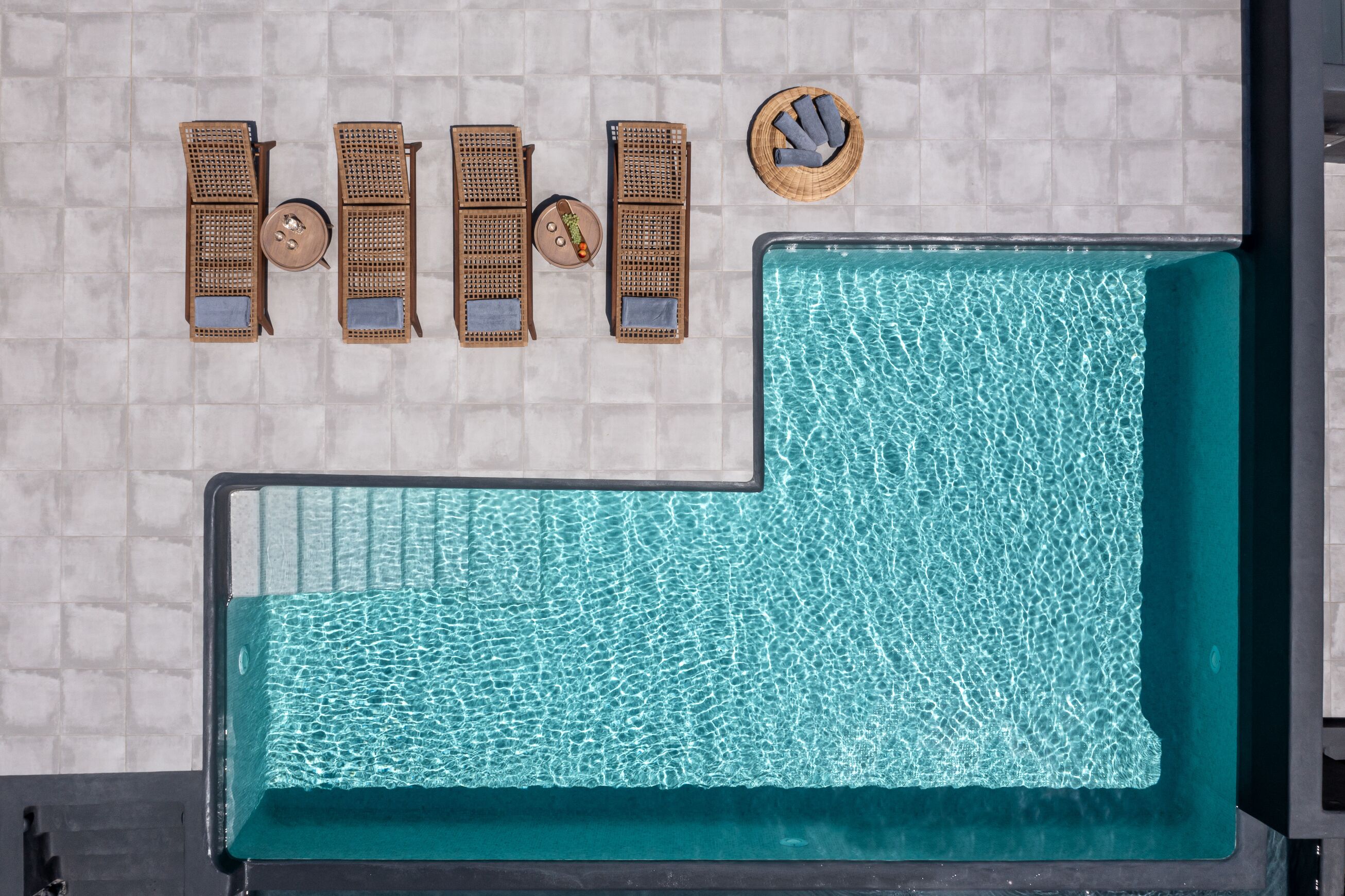 Uma piscina infinita com um recurso de água azul cristalina, cercada por espreguiçadeiras e uma mesa pequena com uma tigela decorativa.