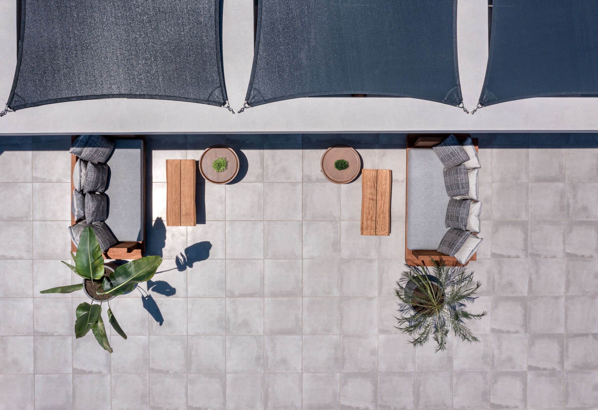 Un espacio al aire libre con dos mesas de madera, dos sillas acolchadas y plantas en macetas.