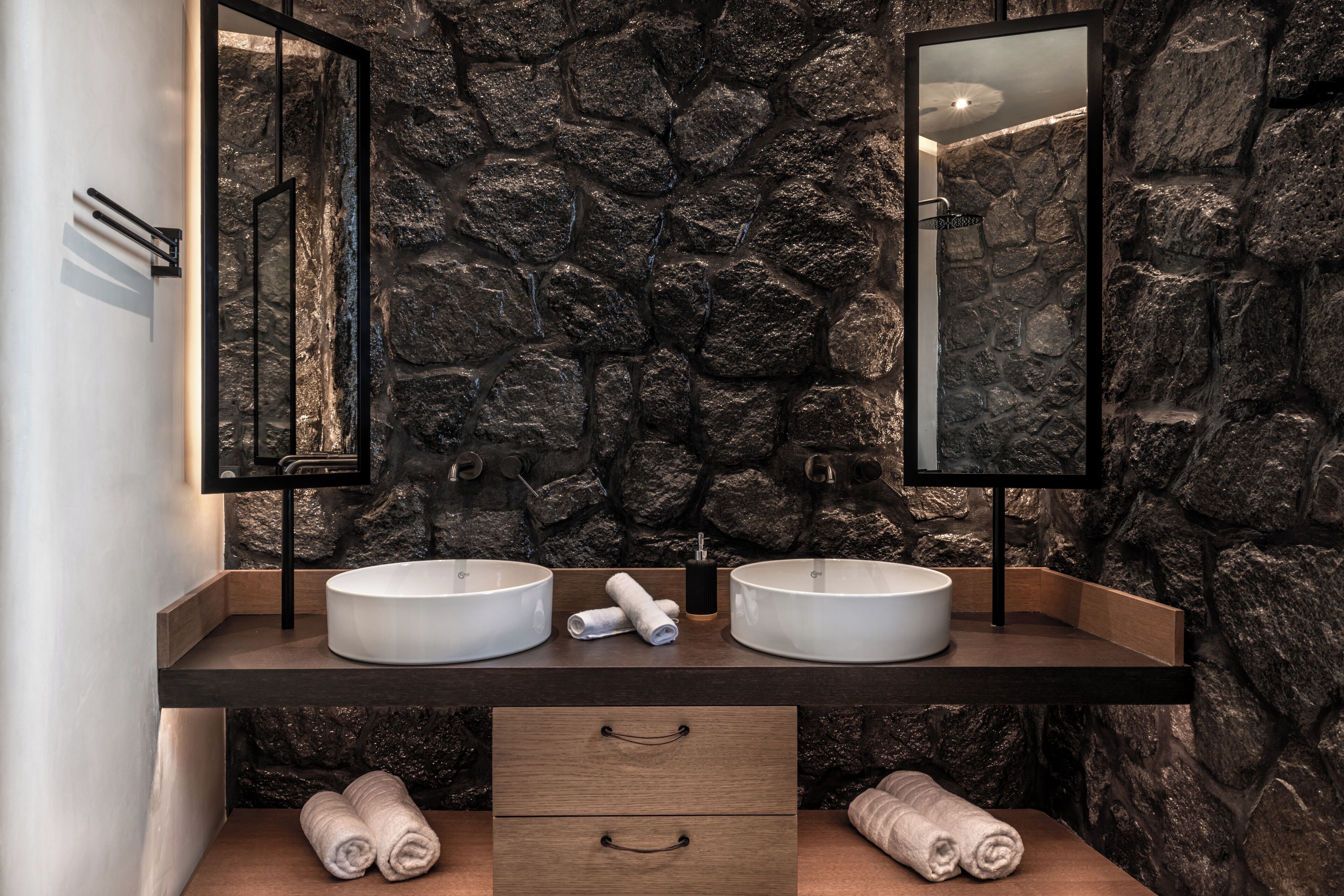 Une salle de bain avec deux lavabos, un meuble-lavabo en bois et un mur en pierre.