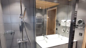 A modern bathroom with a walk-in shower, a large mirror, and a vanity with a sink and towel rack.