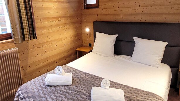 A wooden room with a bed, two pillows, a nightstand, a mirror, and a window with curtains.