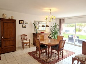 Ein Essbereich mit Holztisch, Stühlen, einer Kandelaber und einem großen Spiegel, mit Blick ins Freie.