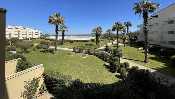 A hotel courtyard with palm trees, a pool, and a view of the ocean.