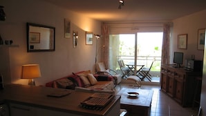 A living room with a sofa, a coffee table, a TV, and a balcony with outdoor furniture.