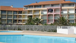 A multi-story hotel with balconies, a swimming pool, and palm trees.